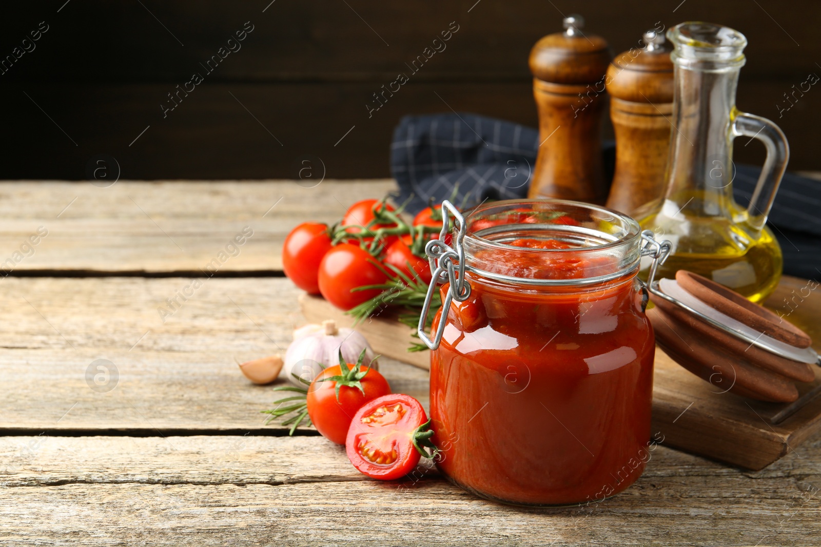 Photo of Homemade tomato sauce in jar and ingredients on wooden table, closeup. Space for text