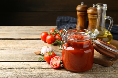 Photo of Homemade tomato sauce in jar and ingredients on wooden table, closeup. Space for text