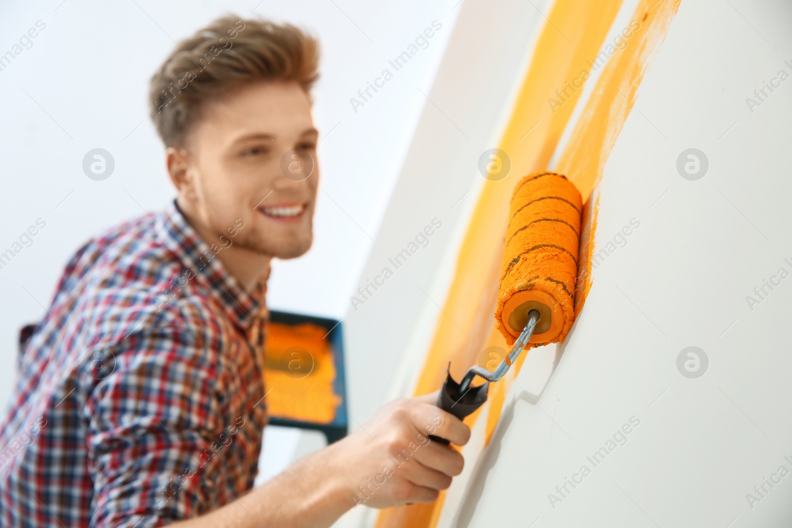 Photo of Happy young man painting wall indoors. Home repair