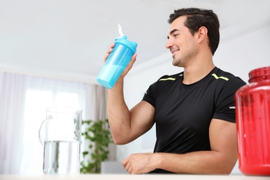 Photo of Young athletic man with protein shake at home, space for text