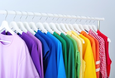 Photo of Rack with rainbow clothes on light background