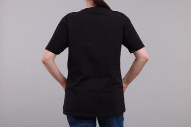 Photo of Woman in stylish black t-shirt light grey on background, back view