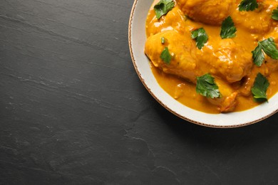 Photo of Tasty chicken curry with parsley on black textured table, top view. Space for text