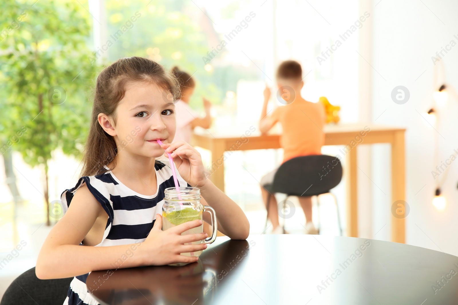 Photo of Little girl with natural lemonade at table indoors