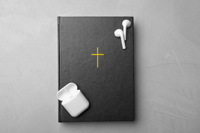 Photo of Bible and earphones on light grey background, top view. Religious audiobook