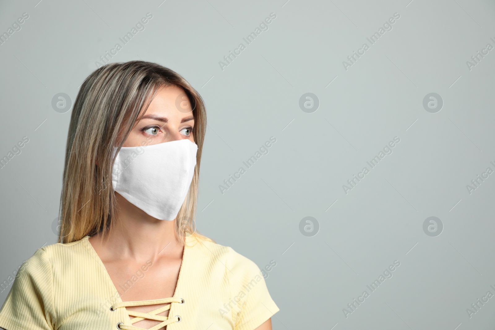 Photo of Young woman in protective face mask on light grey background. Space for text