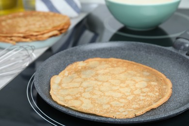 Photo of Delicious thin pancake in frying pan on induction stove, closeup