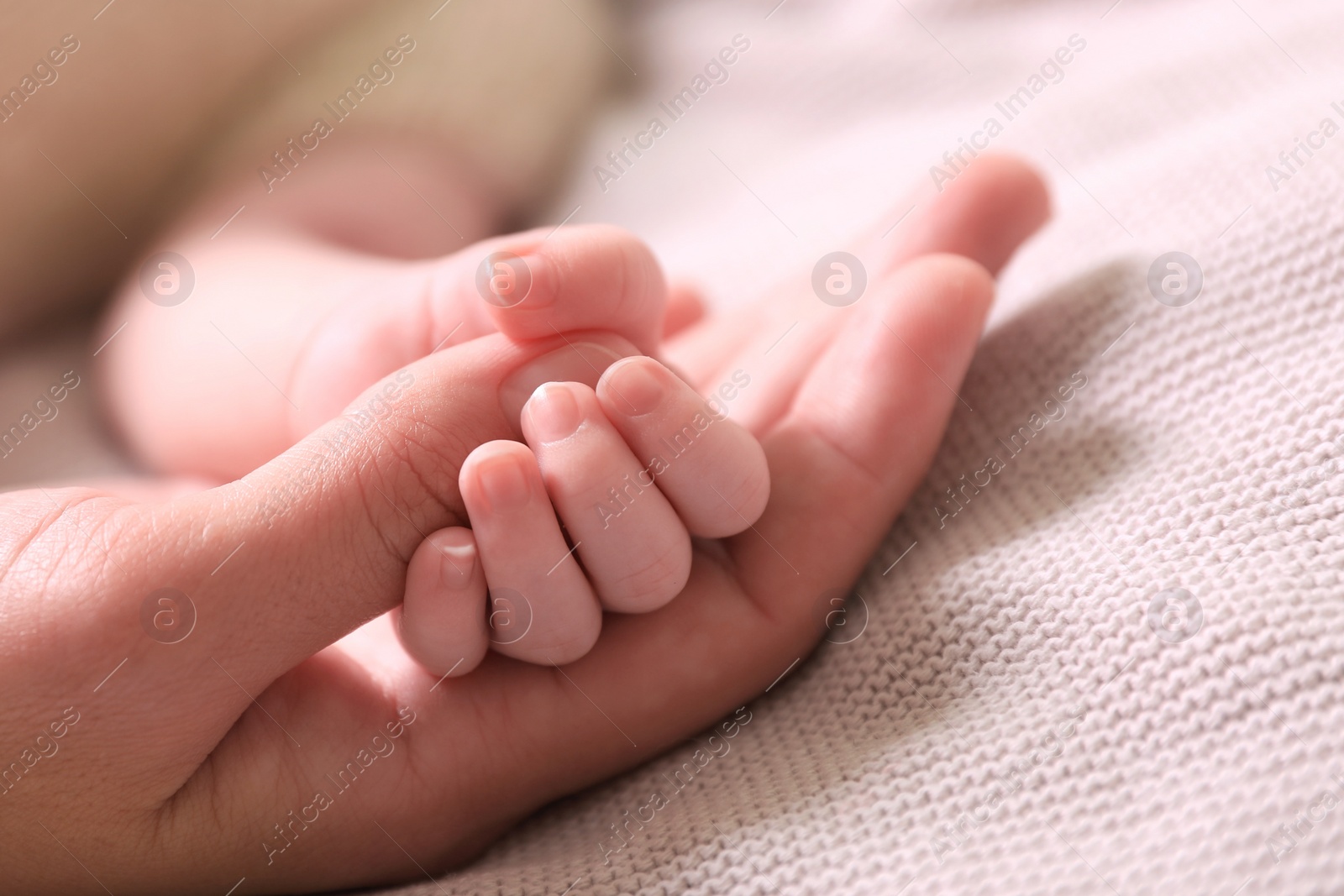 Photo of Mother and her newborn baby on light grey knitted plaid, closeup