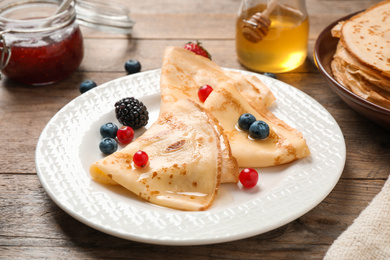 Photo of Delicious thin pancakes with berries on wooden table