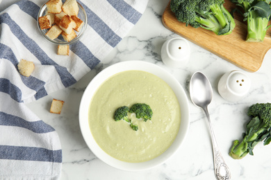 Photo of Delicious broccoli cream soup served on white marble table, flat lay