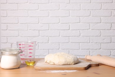 Fresh dough sprinkled with flour and other ingredients on wooden table near white brick wall