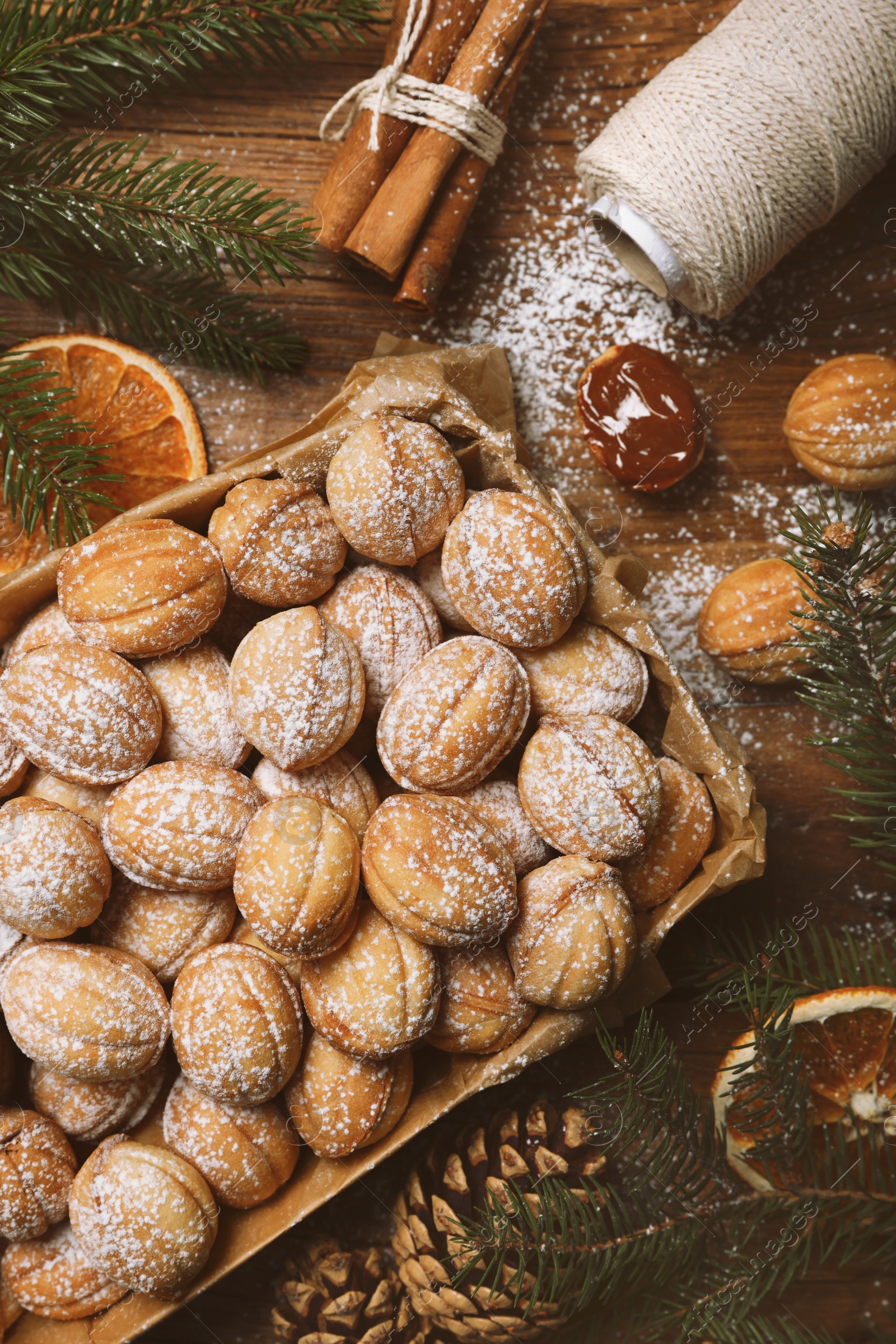 Photo of Delicious nut shaped cookies with boiled condensed milk, dry orange slices and fir tree branches on wooden table, flat lay