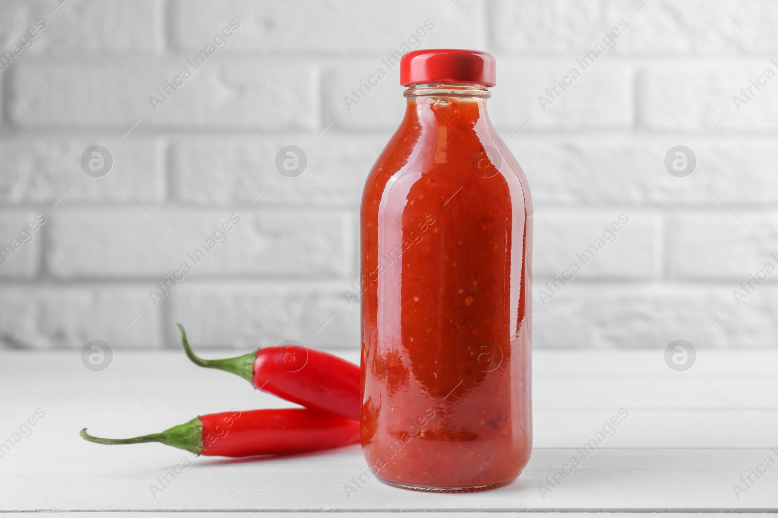 Photo of Spicy chili sauce in bottle and peppers on white wooden table