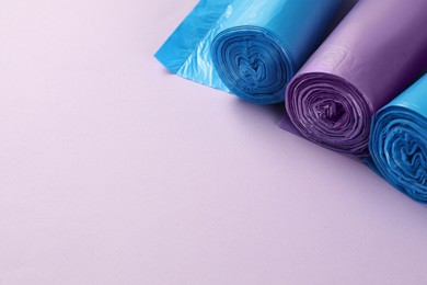 Photo of Rolls of different garbage bags on violet background, space for text