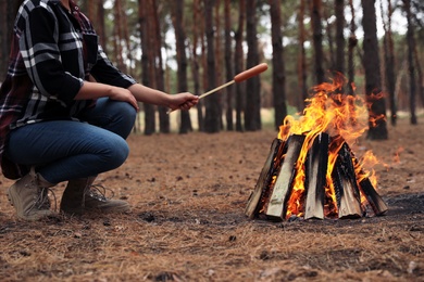 Photo of Woman roasting sausage over burning firewood in forest, closeup