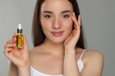 Beautiful young woman with essential oil on light grey background, closeup