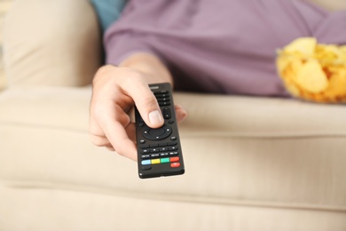 Photo of Man with remote control watching TV on sofa, closeup