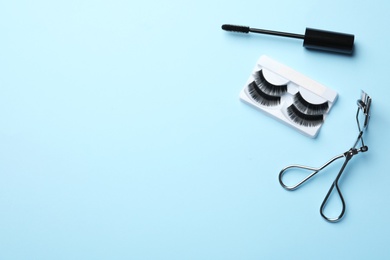 Photo of False eyelashes, curler and mascara on light blue background, flat lay. Space for text