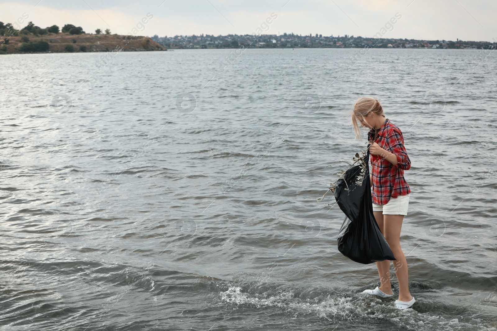 Photo of Woman with trash bag collecting garbage on beach. Space for text