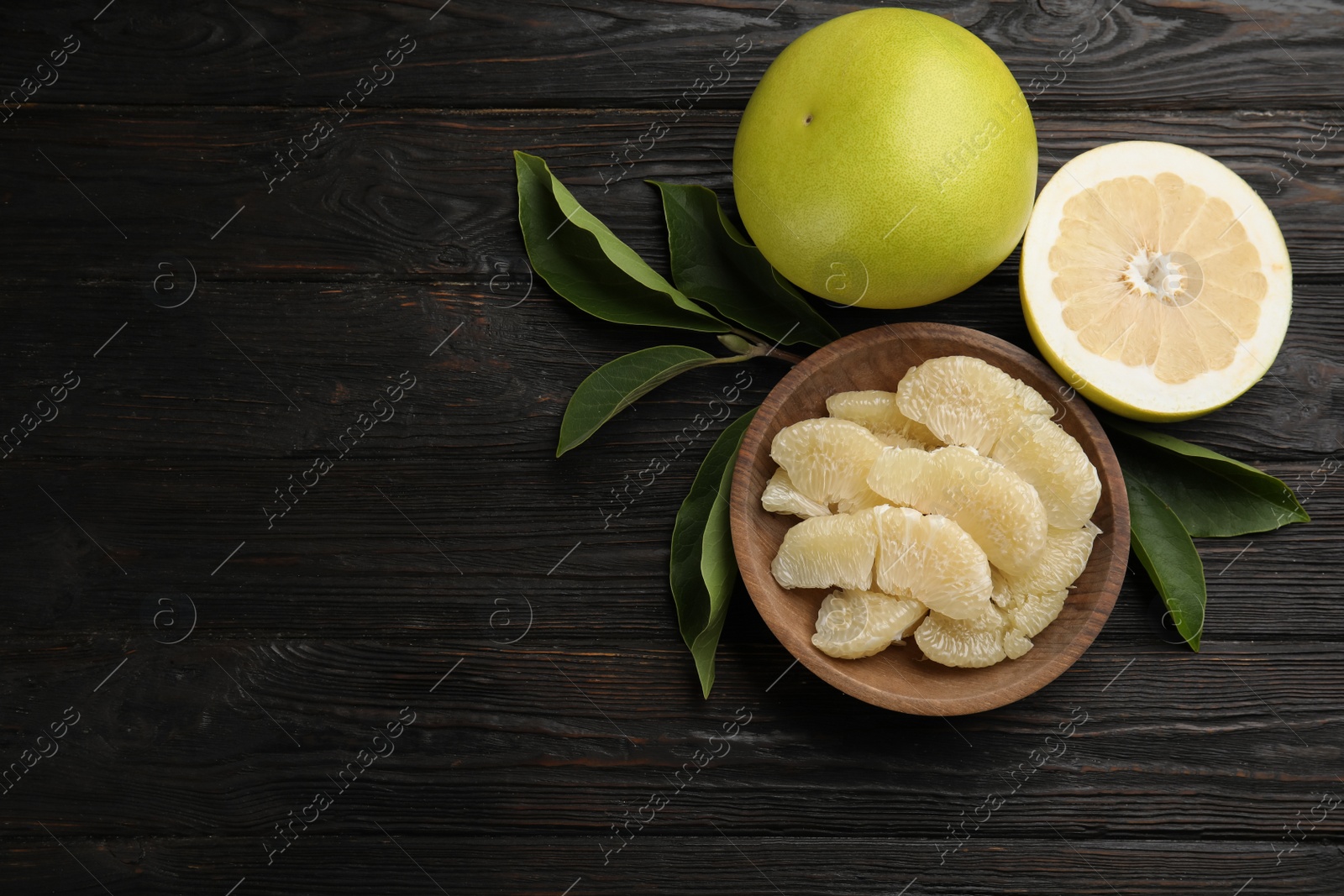 Photo of Fresh cut and whole pomelo fruits on black wooden table, flat lay. Space for text