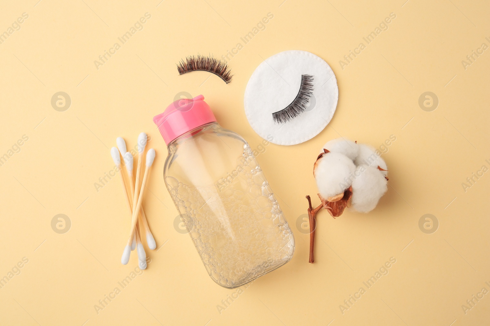 Photo of Bottle of makeup remover, cotton flower, pad, swabs and false eyelashes on yellow background, flat lay