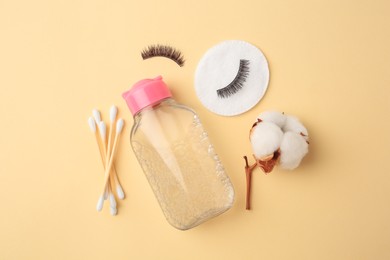 Bottle of makeup remover, cotton flower, pad, swabs and false eyelashes on yellow background, flat lay