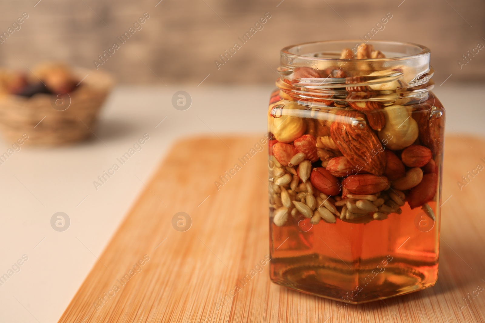 Photo of Different nuts with honey in jar on wooden table, closeup. Space for text