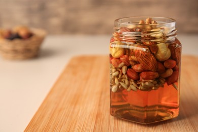 Photo of Different nuts with honey in jar on wooden table, closeup. Space for text