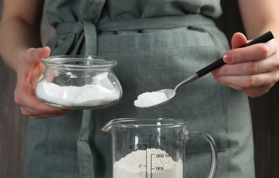 Woman adding baking powder into measuring cup, closeup