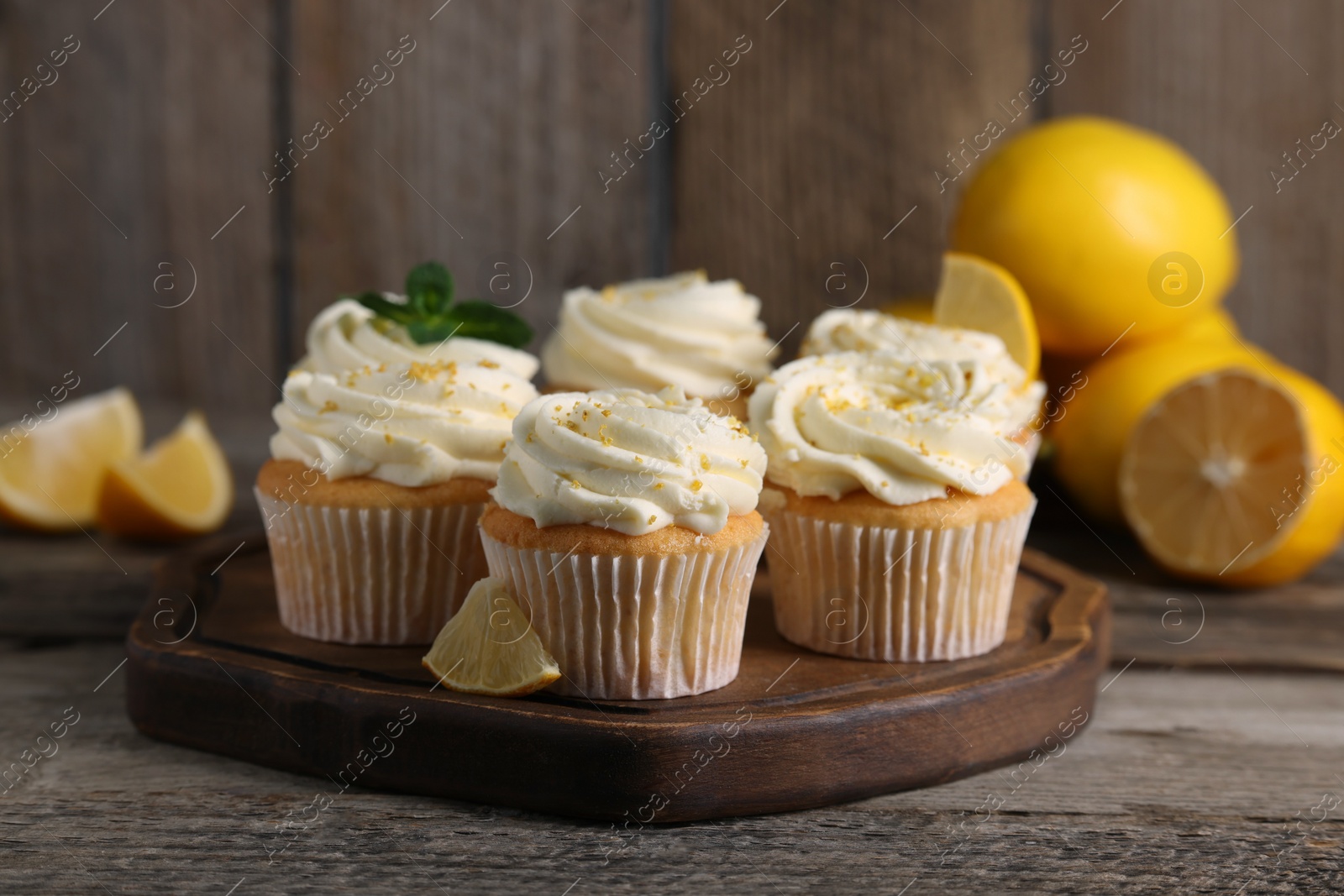 Photo of Delicious cupcakes with white cream and lemon zest on wooden table, closeup