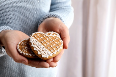 Woman holding tasty heart shaped gingerbread cookies on light background, closeup. Space for text