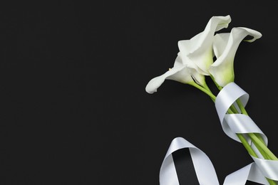 Photo of Beautiful calla lilies and white ribbon on black background, flat lay with space for text. Funeral symbol