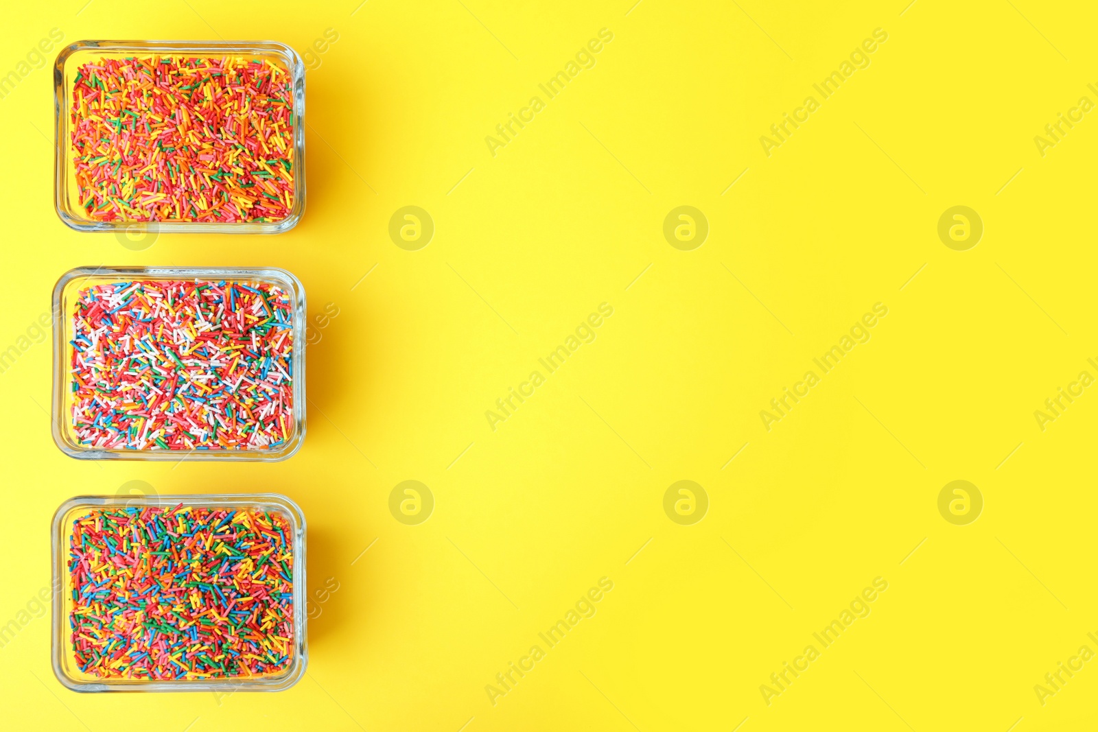 Photo of Colorful sprinkles in bowls on yellow background, flat lay with space for text. Confectionery decor