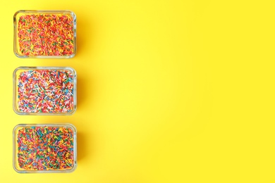 Photo of Colorful sprinkles in bowls on yellow background, flat lay with space for text. Confectionery decor