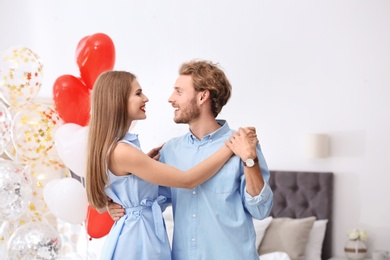 Photo of Young couple with air balloons in bedroom. Celebration of Saint Valentine's Day