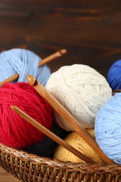 Photo of Clews of colorful knitting threads and crochet hooks in wicker basket, closeup