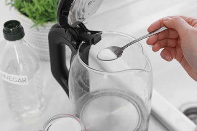Woman adding baking soda into electric kettle in kitchen, closeup