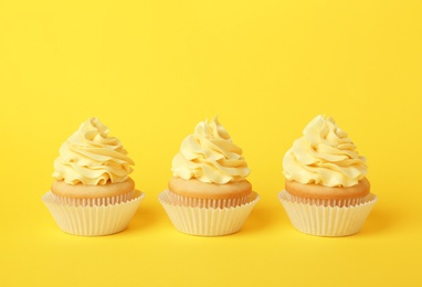 Tasty cupcakes with cream on yellow background