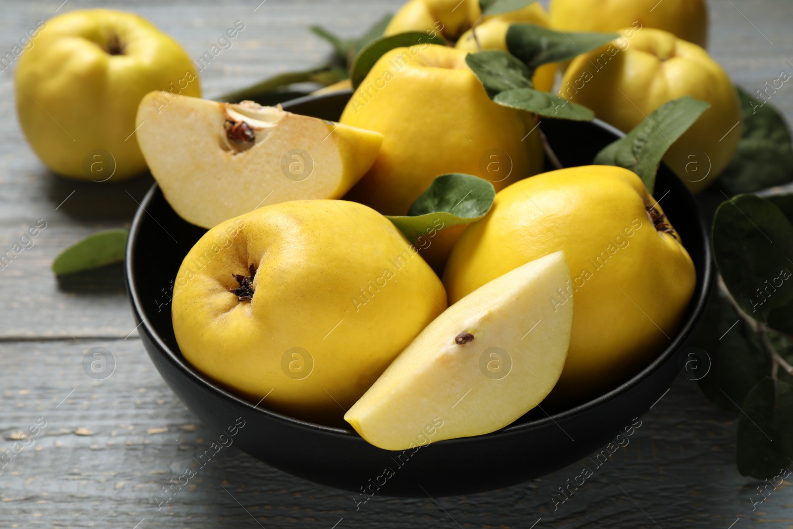 Photo of Fresh ripe organic quinces with leaves on grey wooden table, closeup