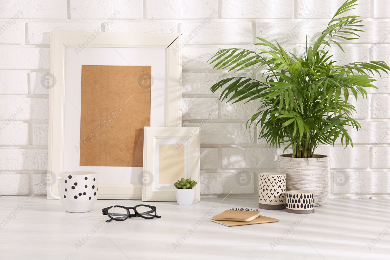 Photo of Stylish office workplace. Decor elements, cup, glasses and notebooks on white table near brick wall