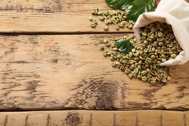 Sackcloth bag with green coffee beans and leaves on wooden table, above view. Space for text