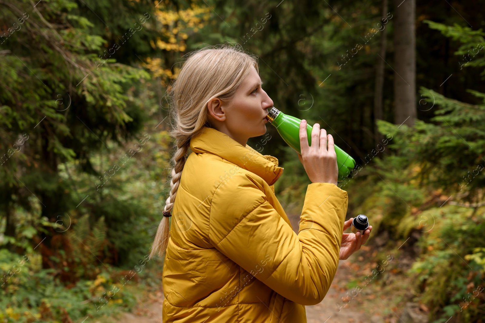 Photo of Young woman drinking hot beverage from thermo bottle in autumn forest