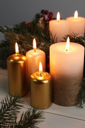 Photo of Different burning candles and Christmas decor on white wooden table
