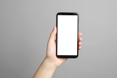 Woman holding smartphone with blank screen on grey background, closeup. Mockup for design