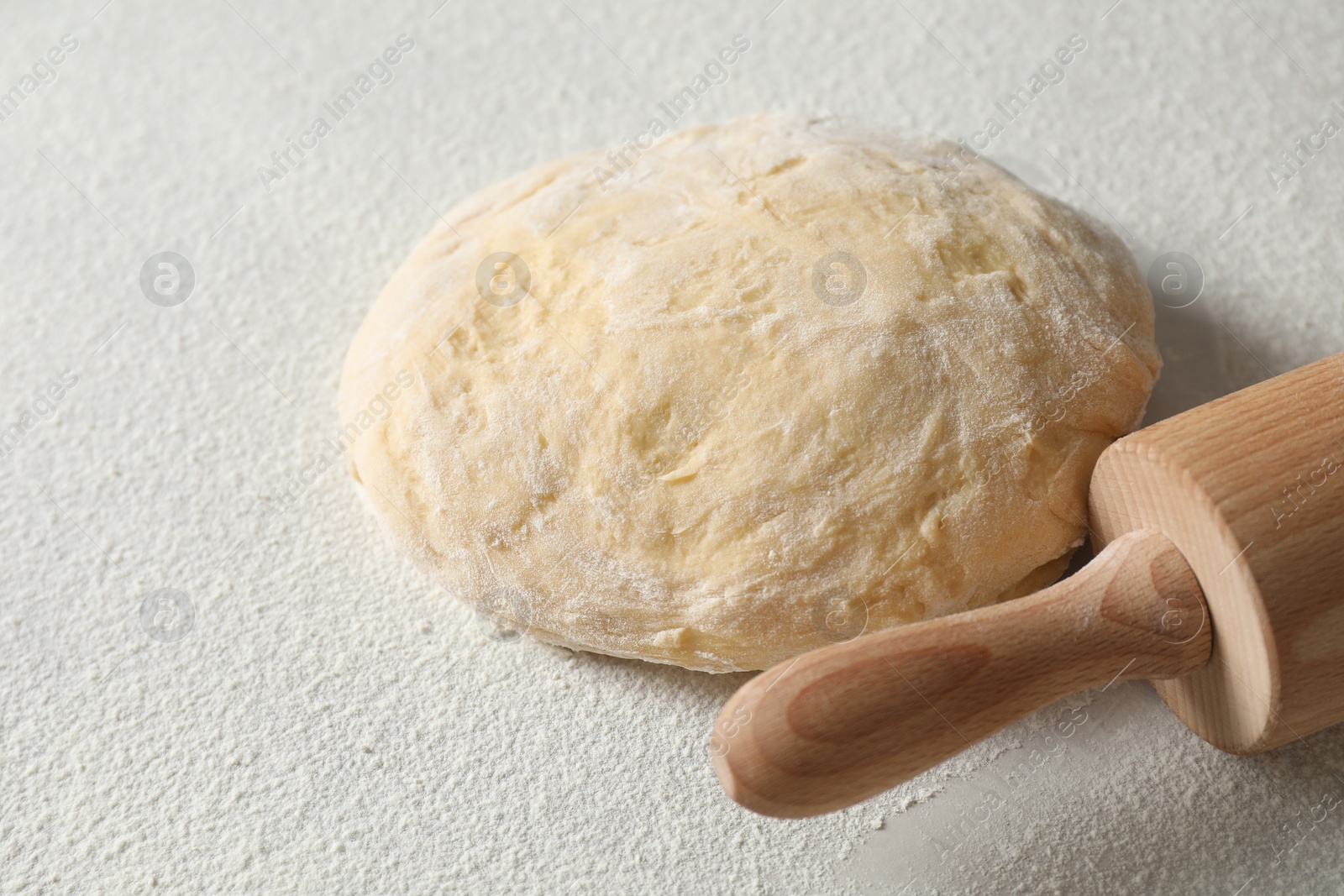 Photo of Raw dough and rolling pin on white table, closeup