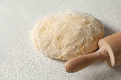 Photo of Raw dough and rolling pin on white table, closeup