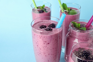 Photo of Delicious blackberry smoothie in different glassware on light blue background