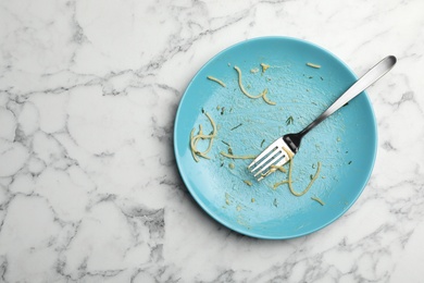 Photo of Dirty plate with food leftovers and fork on marble background, top view. Space for text