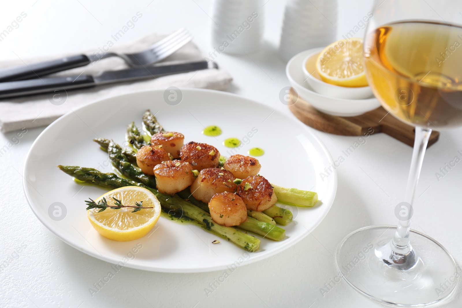 Photo of Delicious fried scallops with asparagus, lemon and thyme served on white table