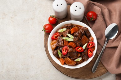 Delicious beef stew with carrots, chili peppers, green onions and potatoes served on white textured table, flat lay. Space for text